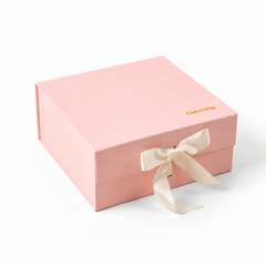 A light pink rectangular gift box with a cream satin ribbon tied in a bow on the front and small gold 'Unboxing' text on the top right, photographed on a clean white background.